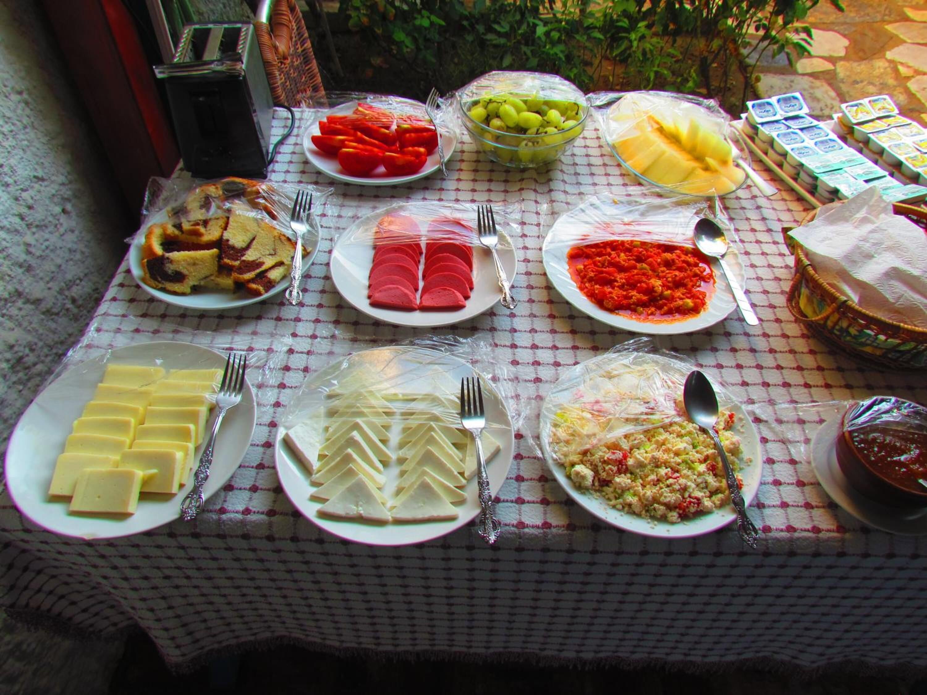 A table with various food items and condiments, including sliced tomatoes, grapes, cheese, and pasta.