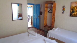 A room with two beds, a wooden wardrobe, a mirror, and a door leading to an outdoor area. - Amazon Antique (Selçuk)