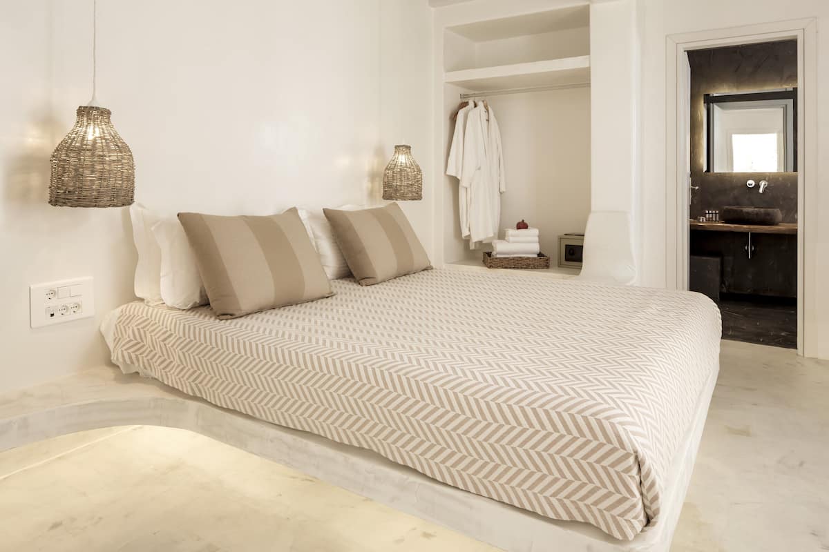 A modern bedroom with a large bed, two bedside lamps, a built-in wardrobe, and a bathroom visible through an open door.