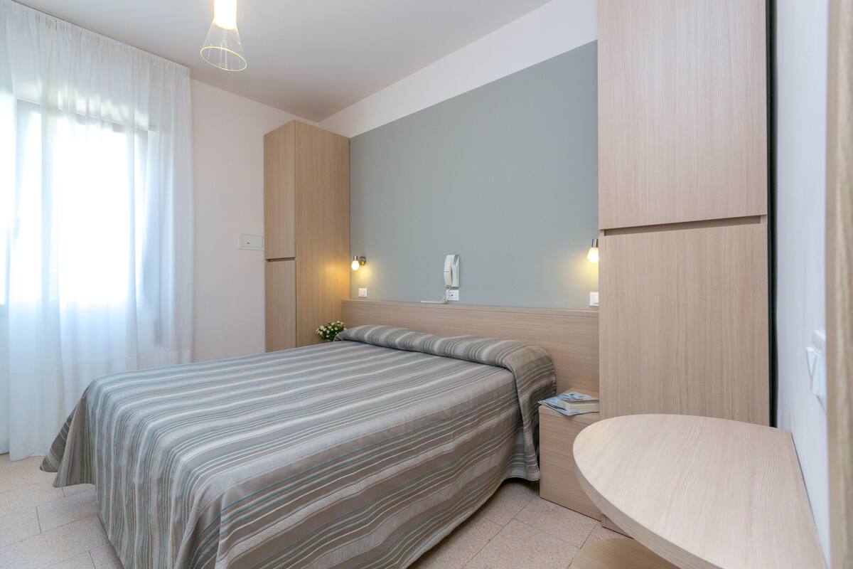 A hotel room with a bed, bedside table, and a mirror.
