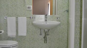 Ein Badezimmer mit grüner Fliesenwand, einem weißen Waschbecken, einem Spiegel über dem Waschbecken, einem weißen Handtuch auf dem Boden und einer Toilette.