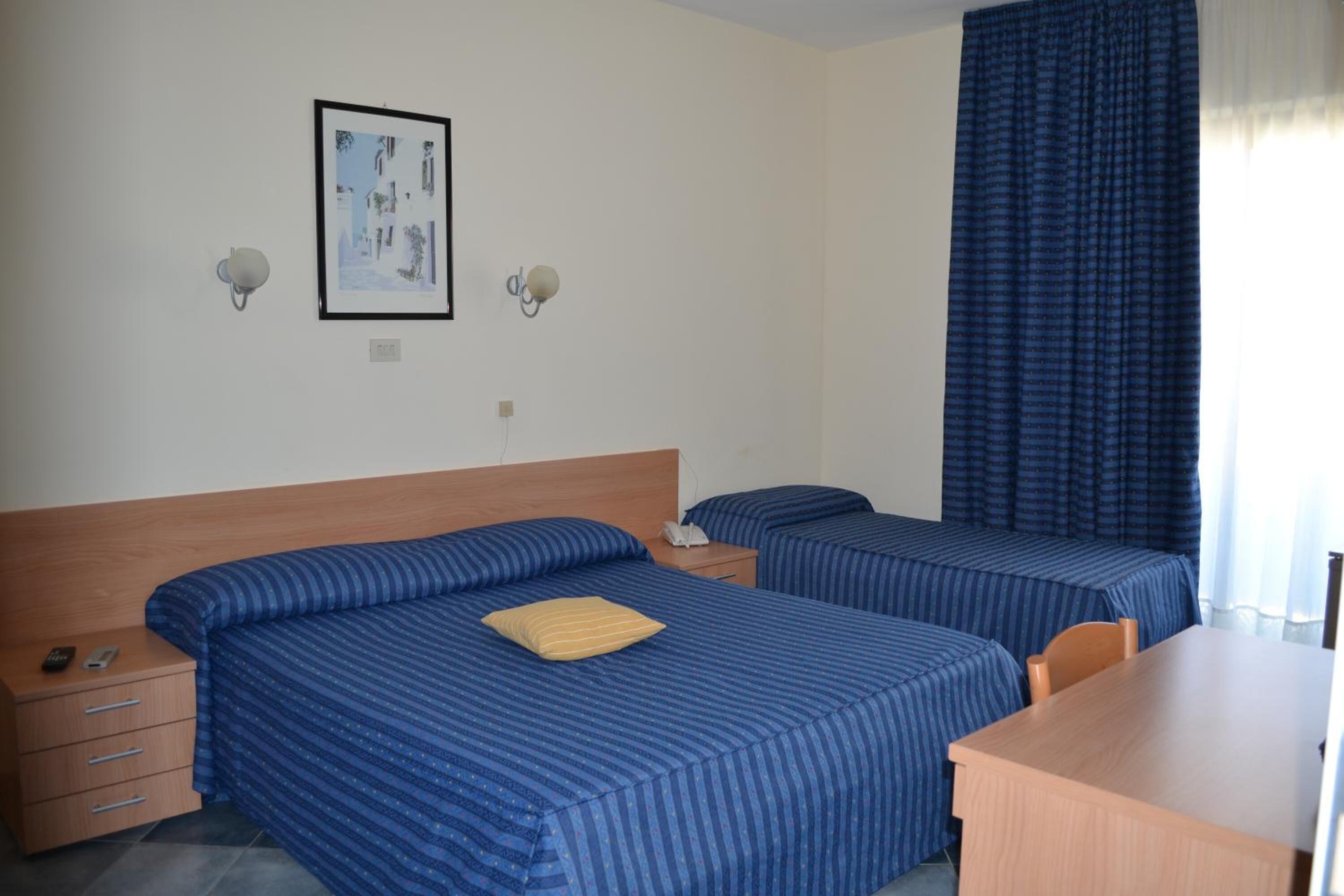 A hotel room with two beds, a wooden headboard, a desk, and a framed picture on the wall.