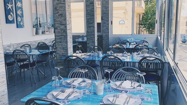 Un restaurant avec une terrasse, des tables bleues et des chaises noires.