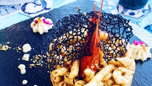 Un plat de fruits de mer accompagné de pâtes et décoré d’un filet, le tout présenté sur une assiette en ardoise sombre.