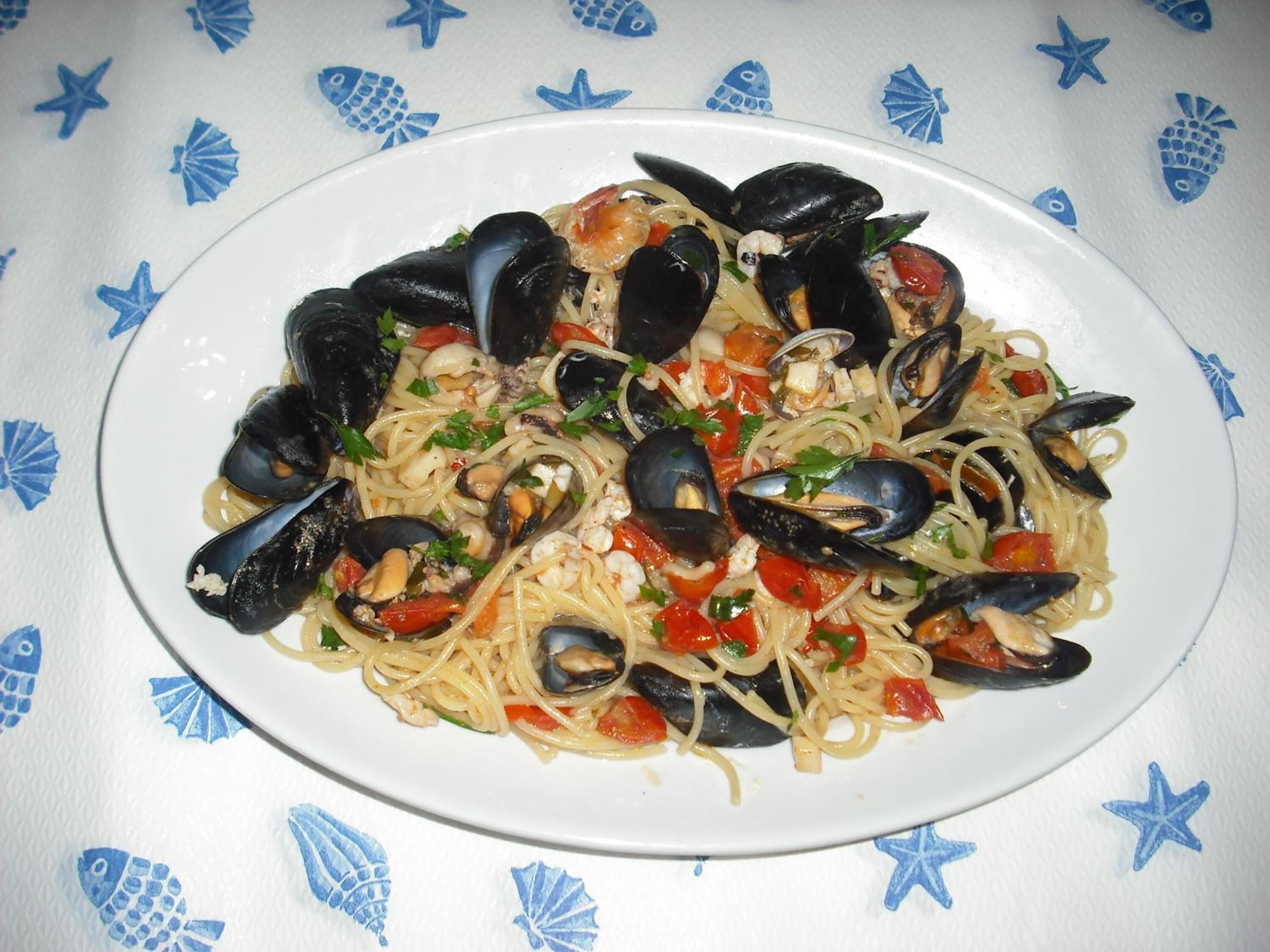 Un piatto di pasta con cozze, pomodori e erbe aromatiche.