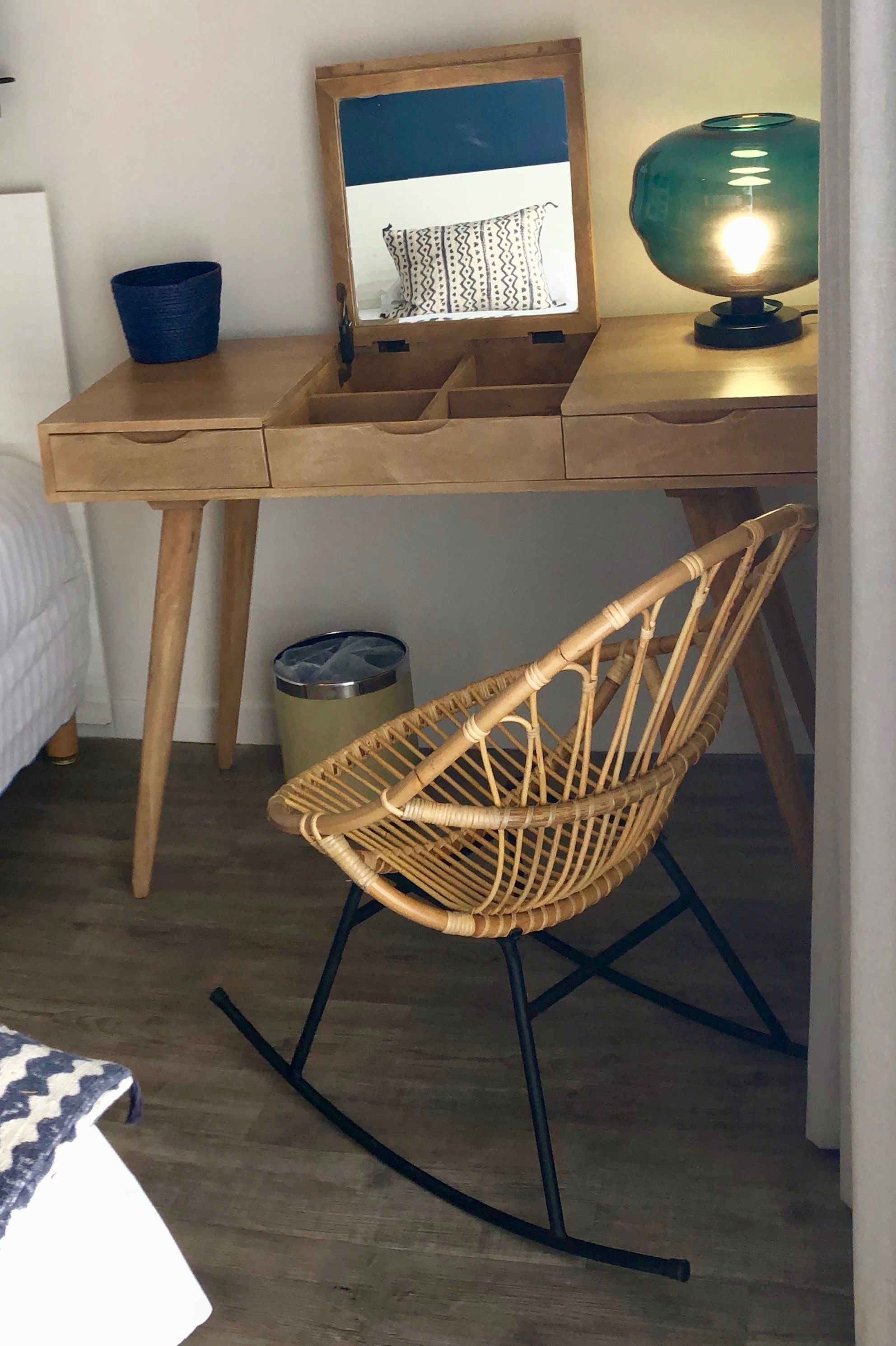 A wooden desk with a framed picture, a blue basket, and a green lamp.