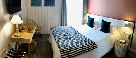 A hotel room with a bed, bedside table, lamp, chair, and a small round table with a phone.
