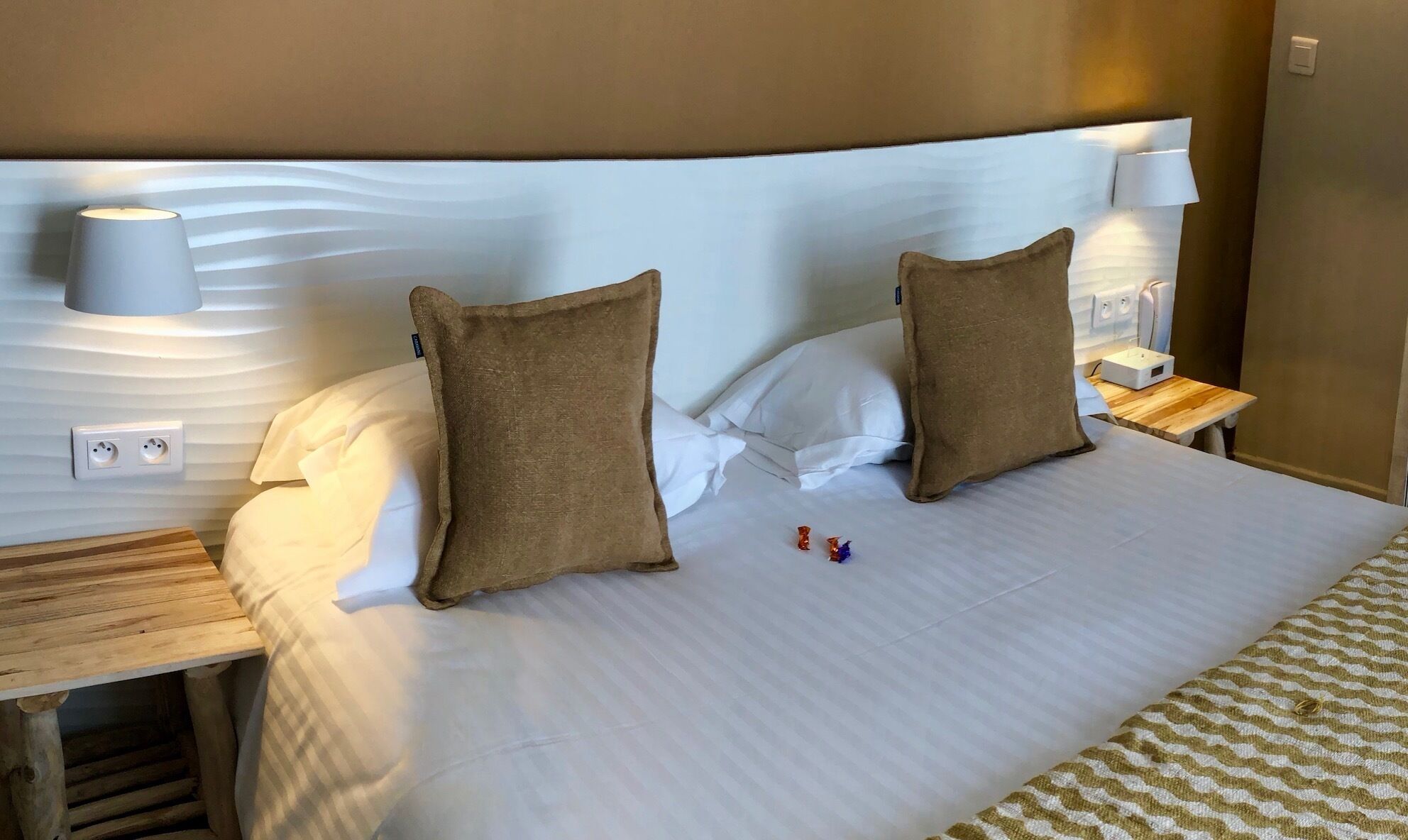 Un lit bien fait avec deux oreillers, une table de chevet avec une lampe et une prise électrique sur le mur.