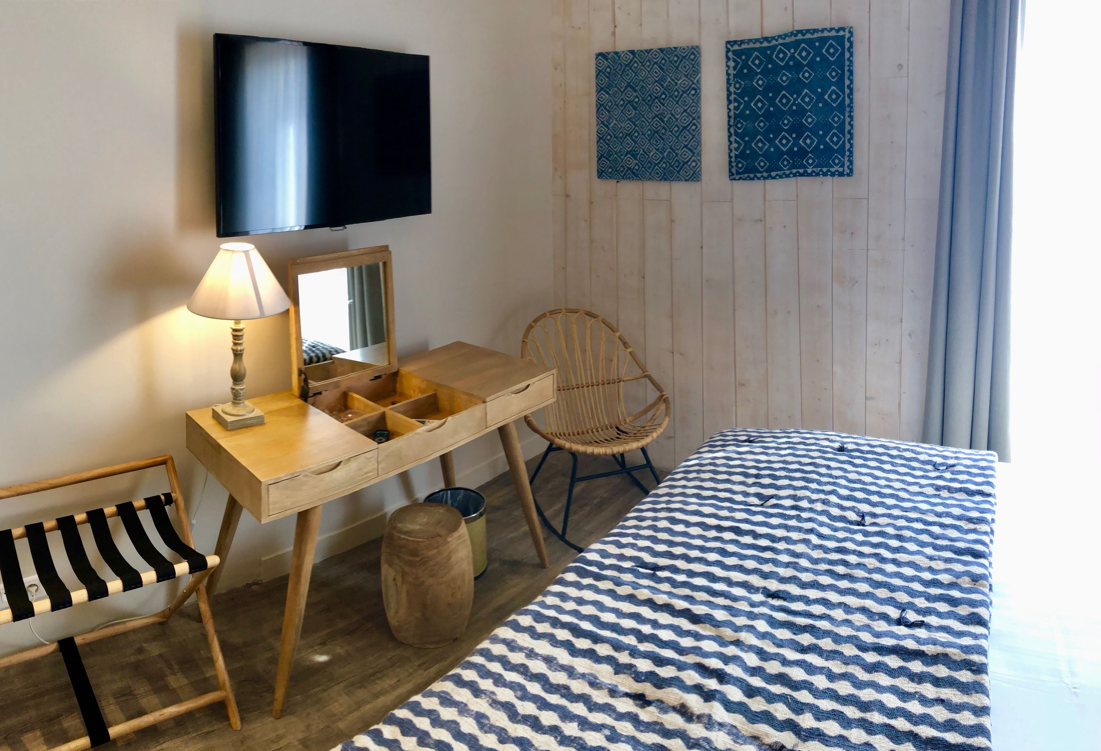 Una camera da letto con un letto, una scrivania con una lampada, una sedia, un televisore e due decorazioni a parete a motivi decorativi.