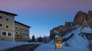 A hotel named "HOTEL CIR" with a sign on a rock, surrounded by snow-covered mountains and a building with multiple windows. - Hotel Cir (Corvara in Badia)