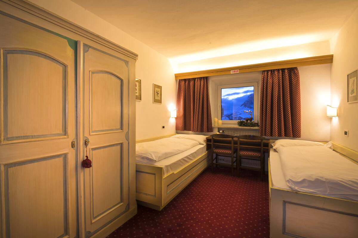 Une chambre d’hôtel avec deux lits simples, un bureau, une chaise, une fenêtre avec des rideaux et une porte avec une poignée.