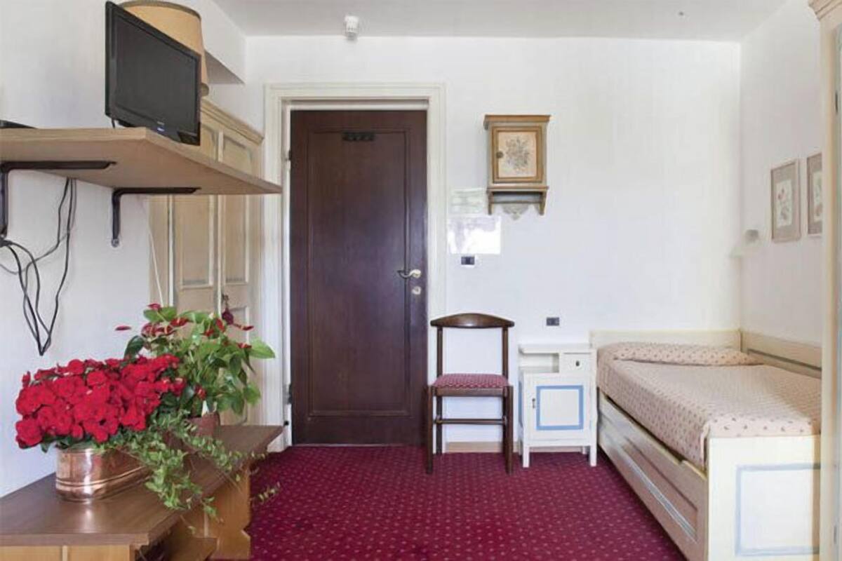 Une pièce comprenant un lit, une chaise, un bureau et un téléviseur posé sur une étagère.