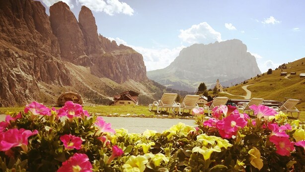A mountainous landscape with a road, a small building, and several lounge chairs. - Hotel Cir (Corvara in Badia)