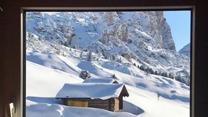 A window view of a snow-covered mountain landscape with a wooden cabin. - Hotel Cir (Corvara in Badia)