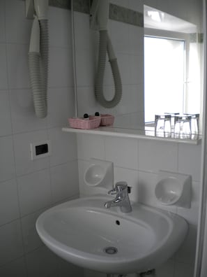 A bathroom with a white sink, two soap dispensers, a mirror, and a window.