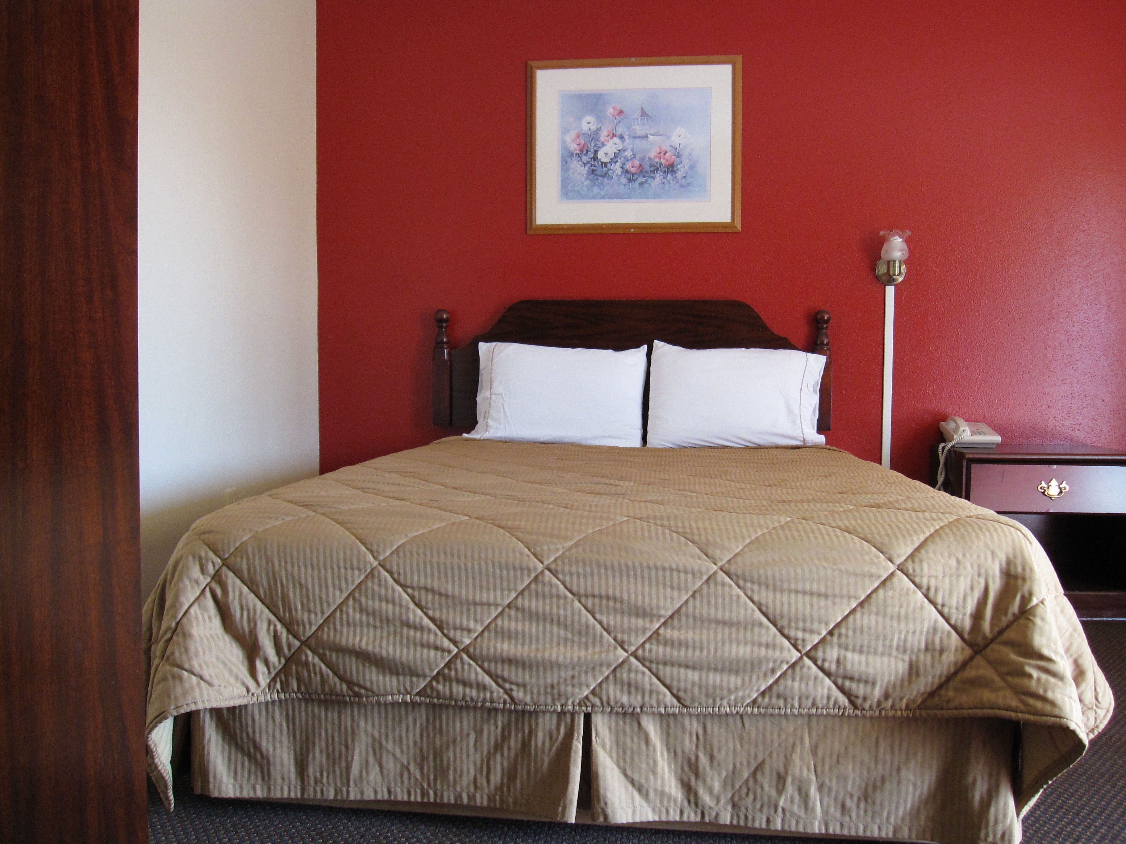 A hotel room with a bed, a nightstand, a lamp, and a painting on the wall.