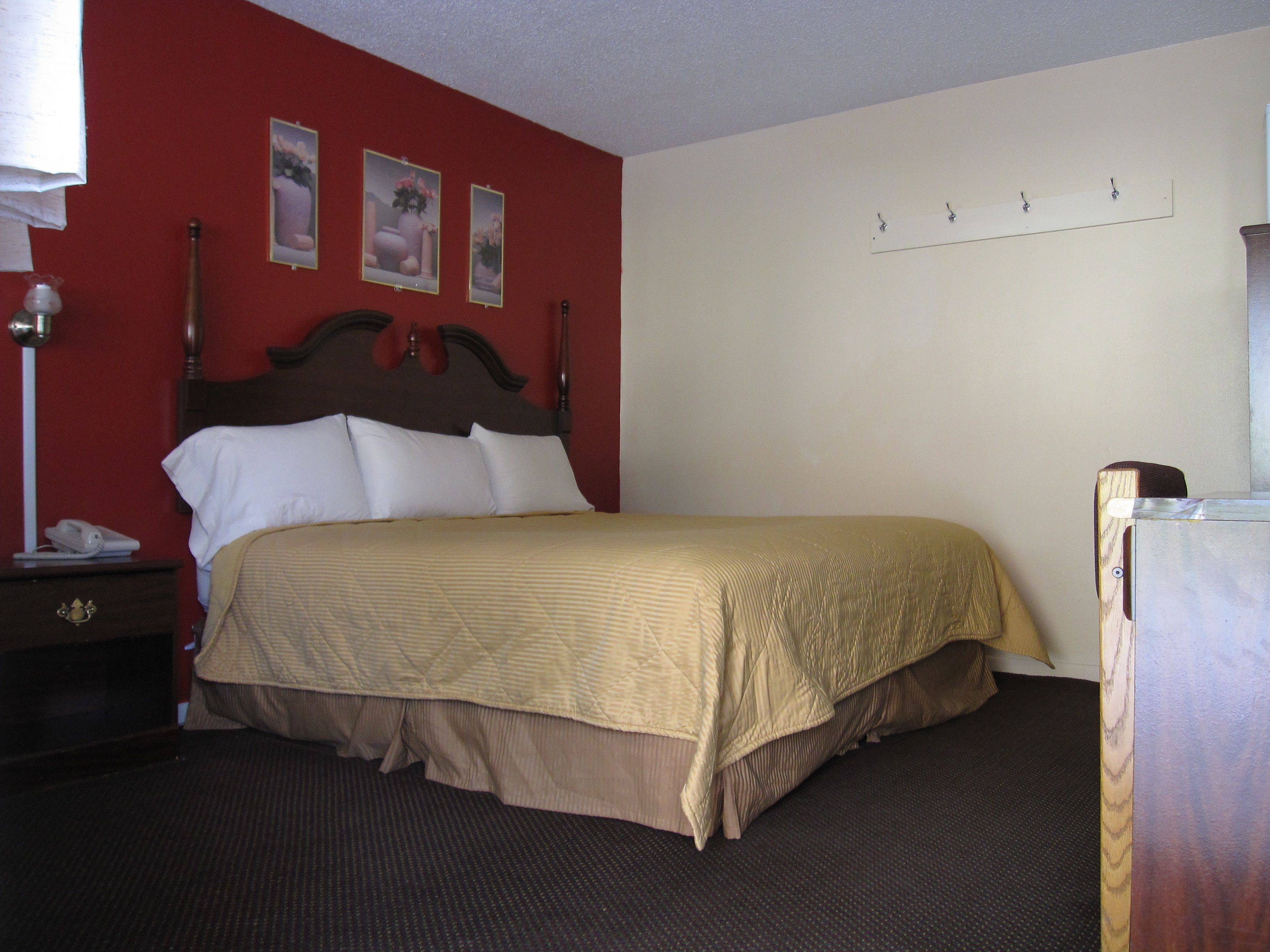 A hotel room with a bed, a nightstand, a lamp, and a wall with three framed pictures.