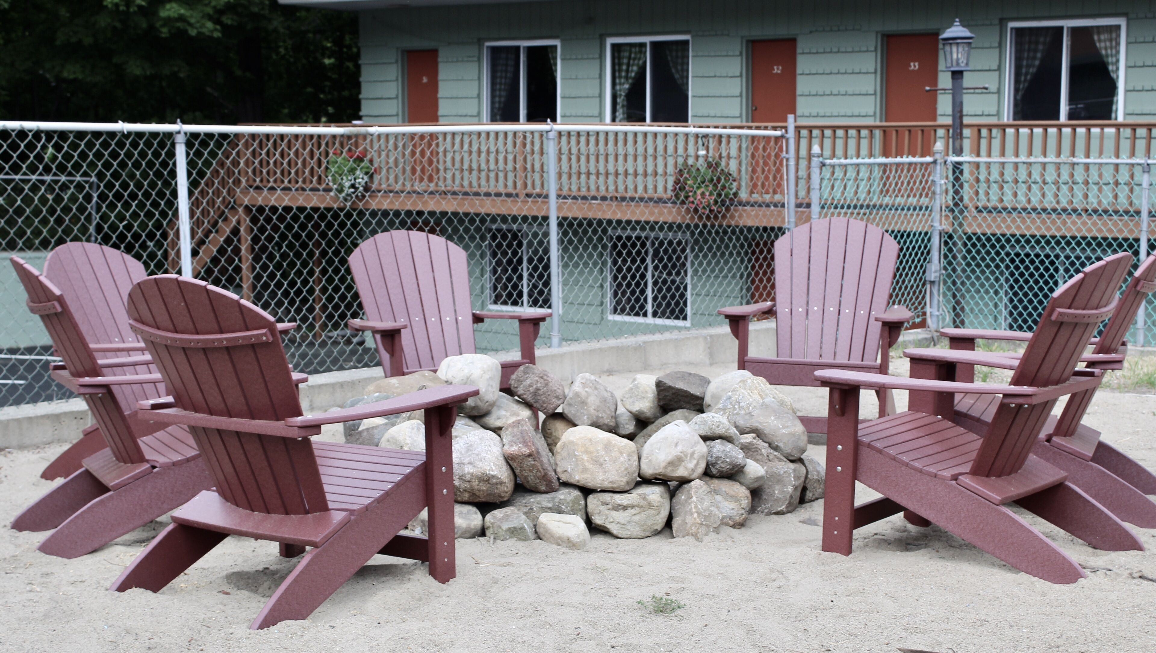 Four Adirondack chairs around a small fire pit, with a building in the background.