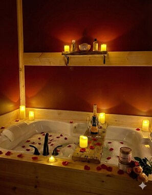 A wooden bathtub with rose petals, candles, and a bottle of champagne.