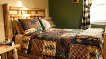 A wooden bed with a quilt, a nightstand with books and a mug, and a green wall with a picture.