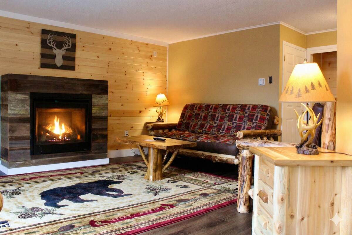 Una sala de estar acogedora con chimenea, un sofá, una mesa de centro y una alfombra con estampado de oso.
