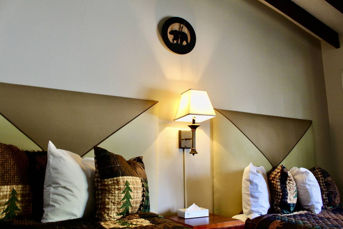 Una habitación de hotel con cama, almohadas, lámpara de noche y un adorno en la pared.