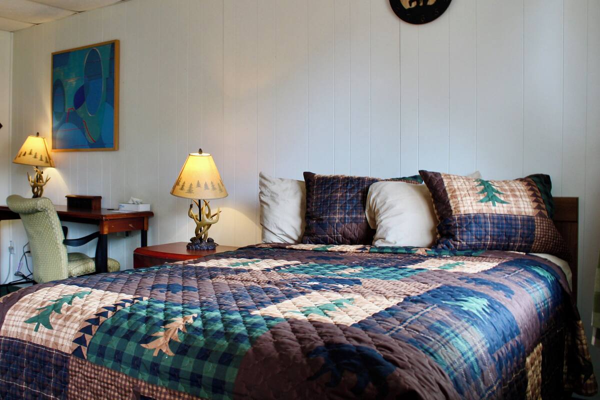 Un dormitorio con una cama grande, una mesita de noche con lámpara, una silla y un reloj de pared.