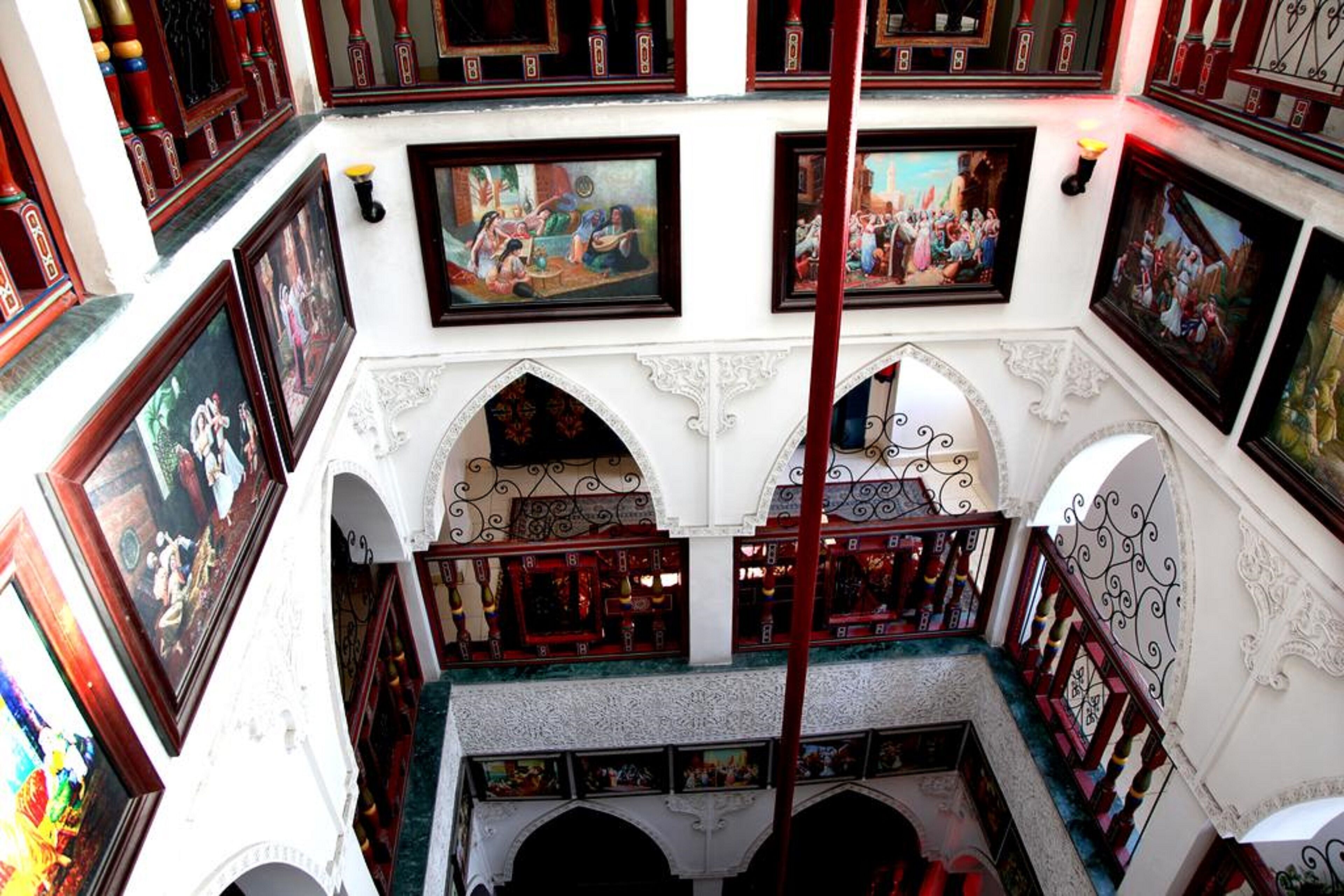 A multi-level interior with ornate railings, framed artwork, and a central staircase.