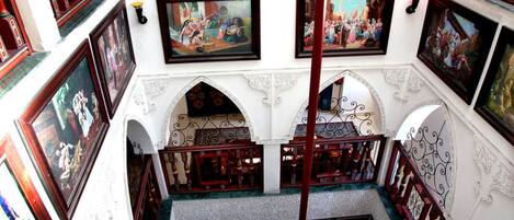 A multi-level interior with ornate railings, framed artwork, and a central staircase.