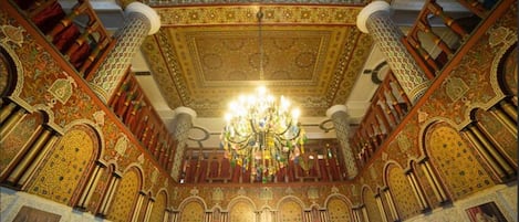 A grand hall with ornate golden ceilings, a large chandelier, and intricate wall designs.