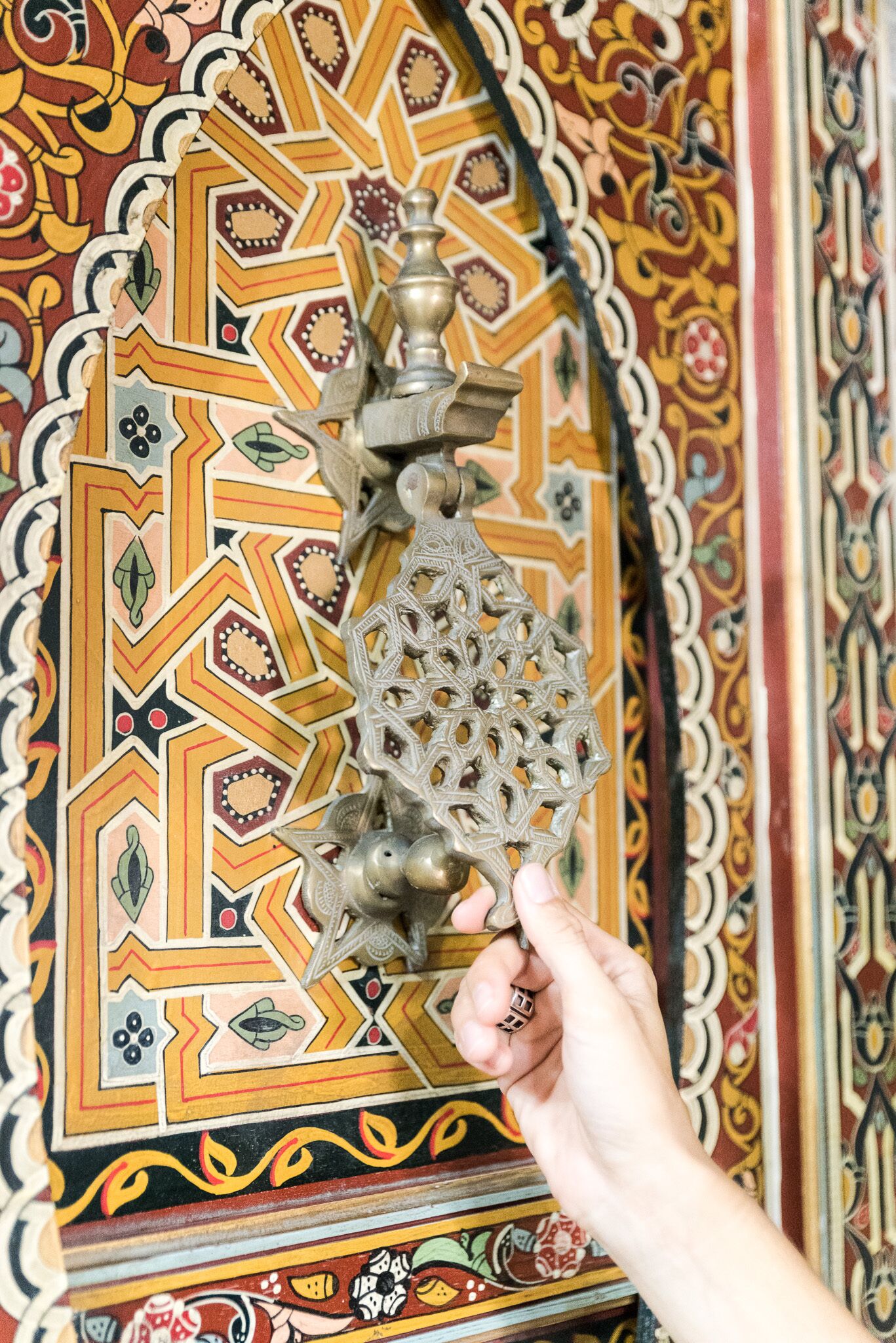 A hand holding a key in front of a decorative door with intricate geometric patterns.