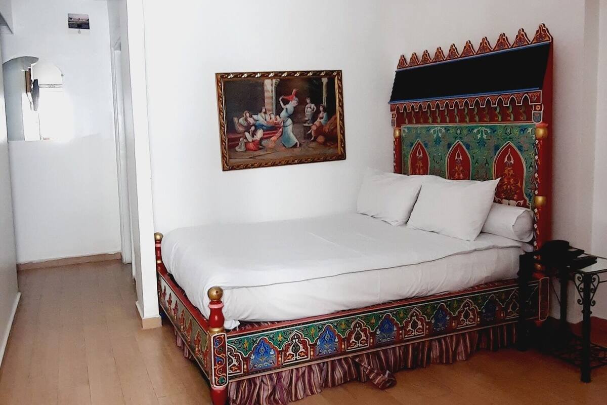 Ein Schlafzimmer mit einem Bett, einer Chandelier, einem Gemälde und einem gemusterten Kopfteil.