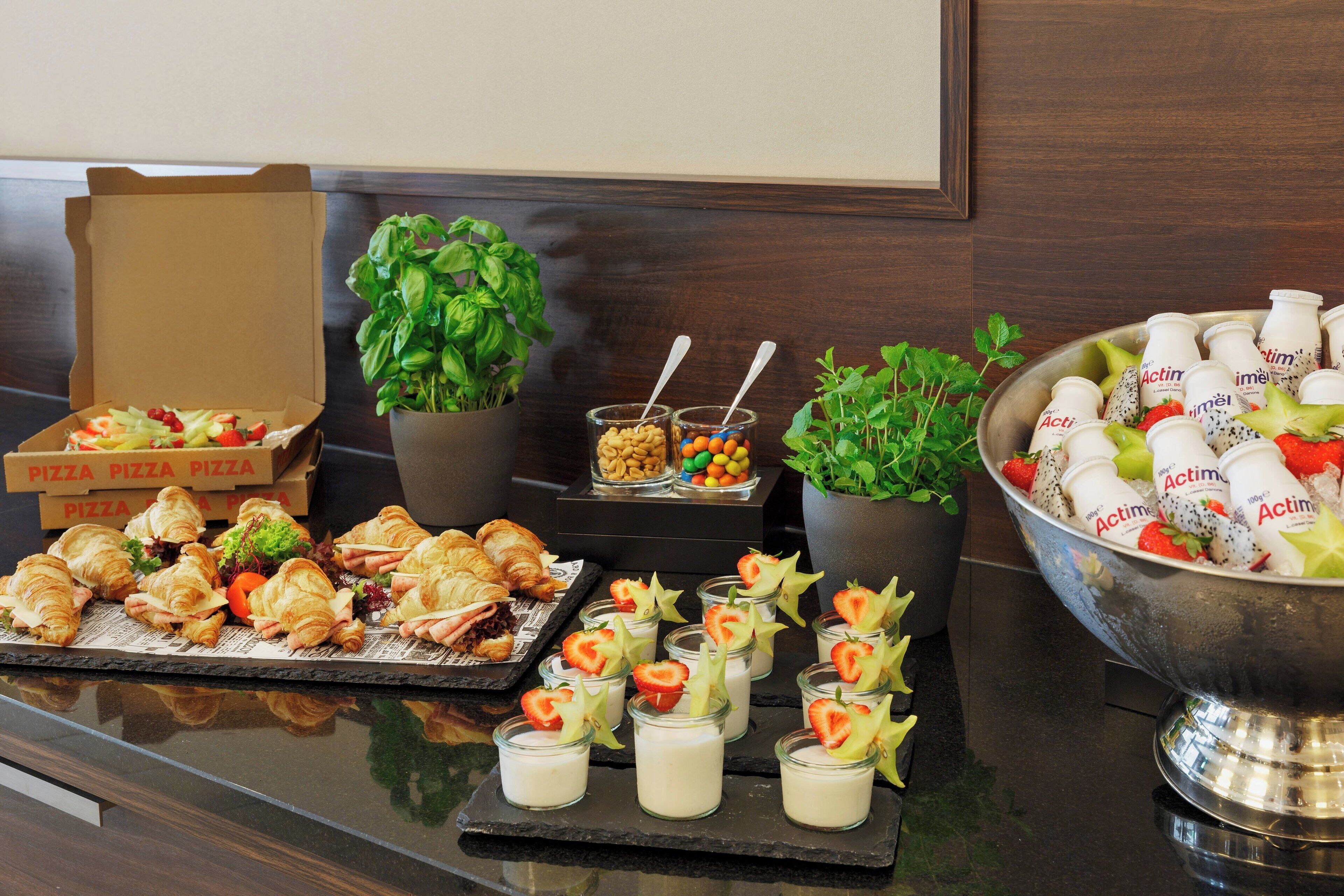 A buffet table with pizza boxes, croissants, and a bowl of yogurt drinks.