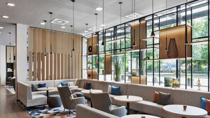 A modern lounge area with sofas, chairs, and round tables, featuring large windows and natural light. - Courtyard München City Ost (Munich)