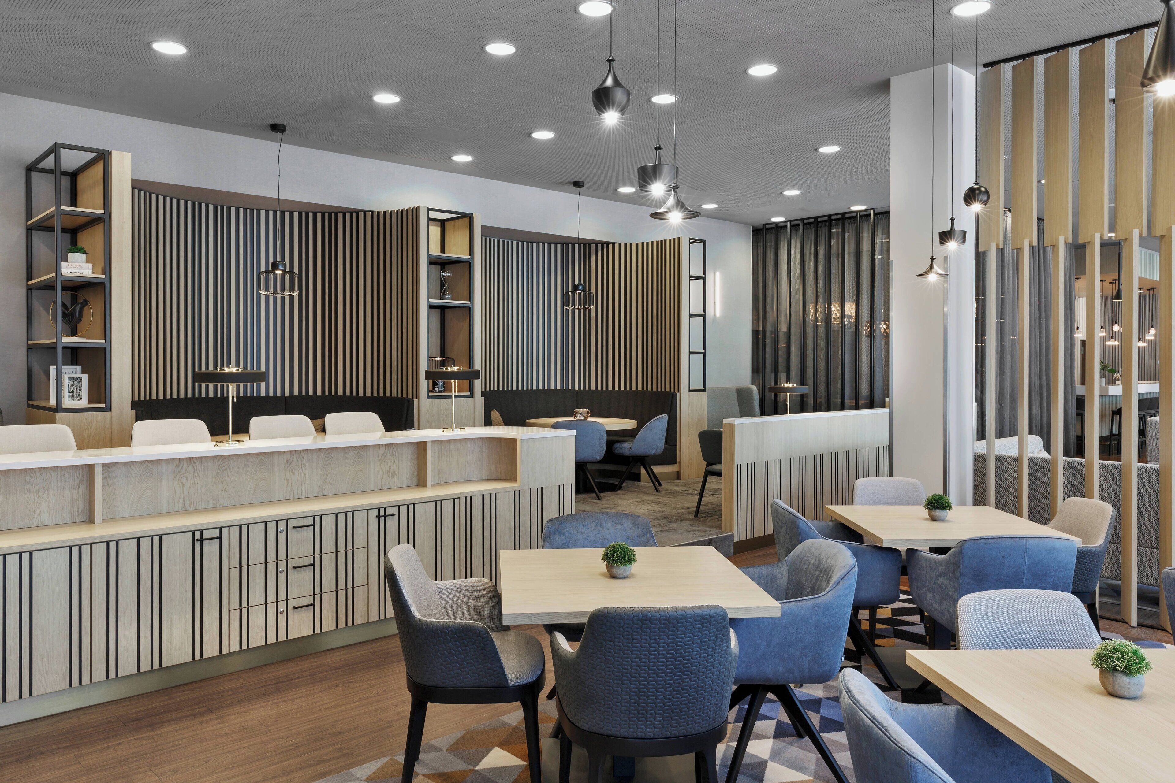A modern restaurant with a long counter, blue upholstered chairs, and pendant lighting.
