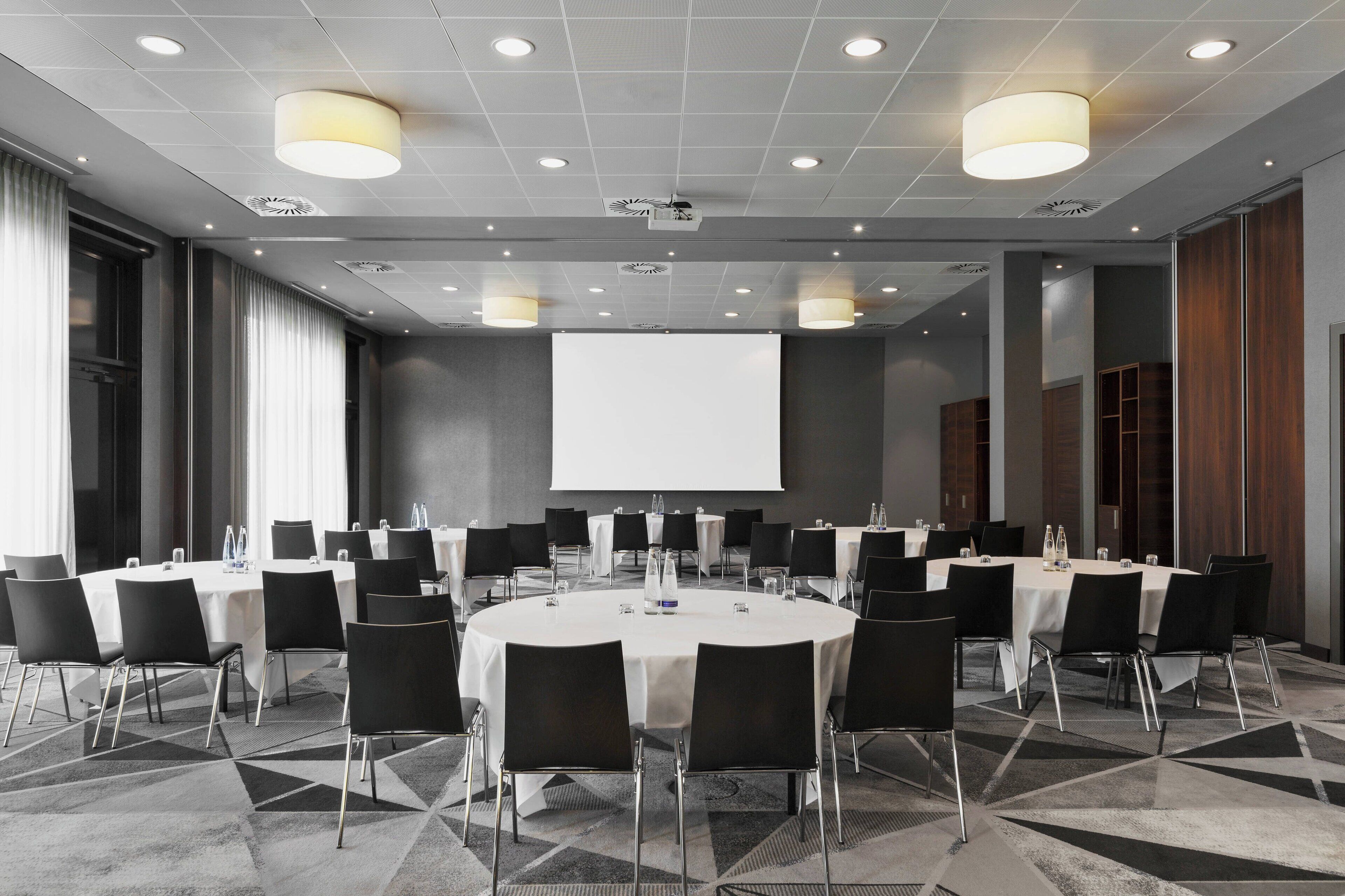 A conference room with round tables, black chairs, and a large screen at the front.