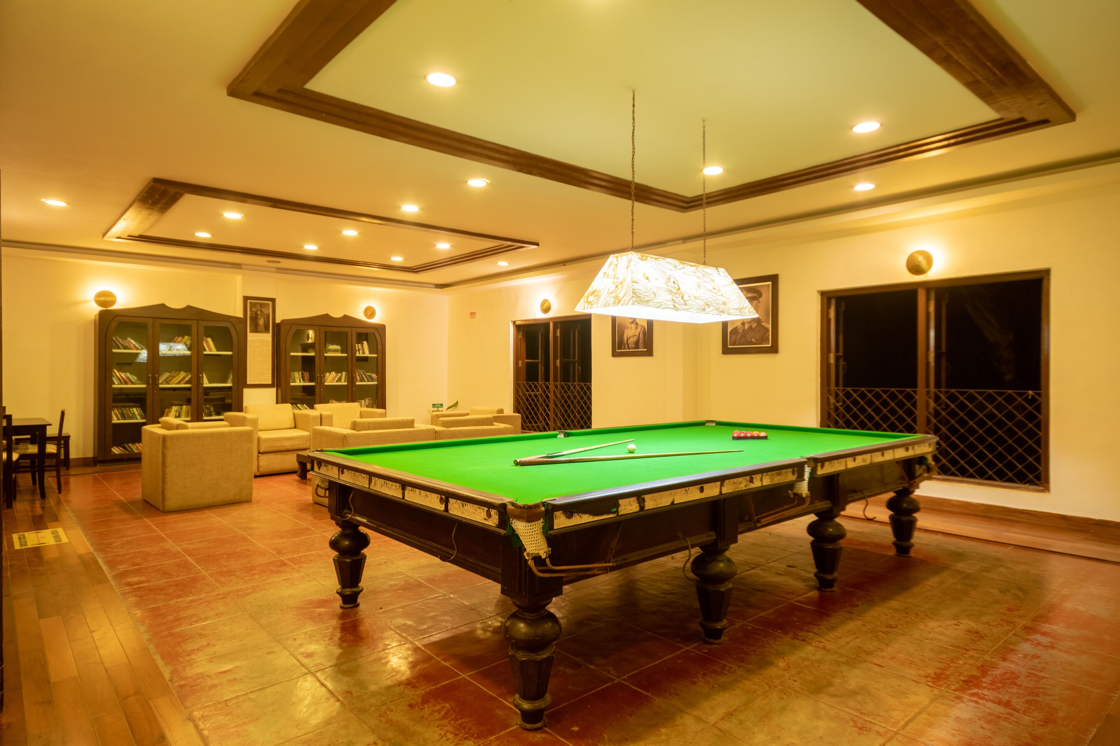 Une table de billard dans une pièce bien éclairée, dotée d’un plafond haut et de bibliothèques intégrées.