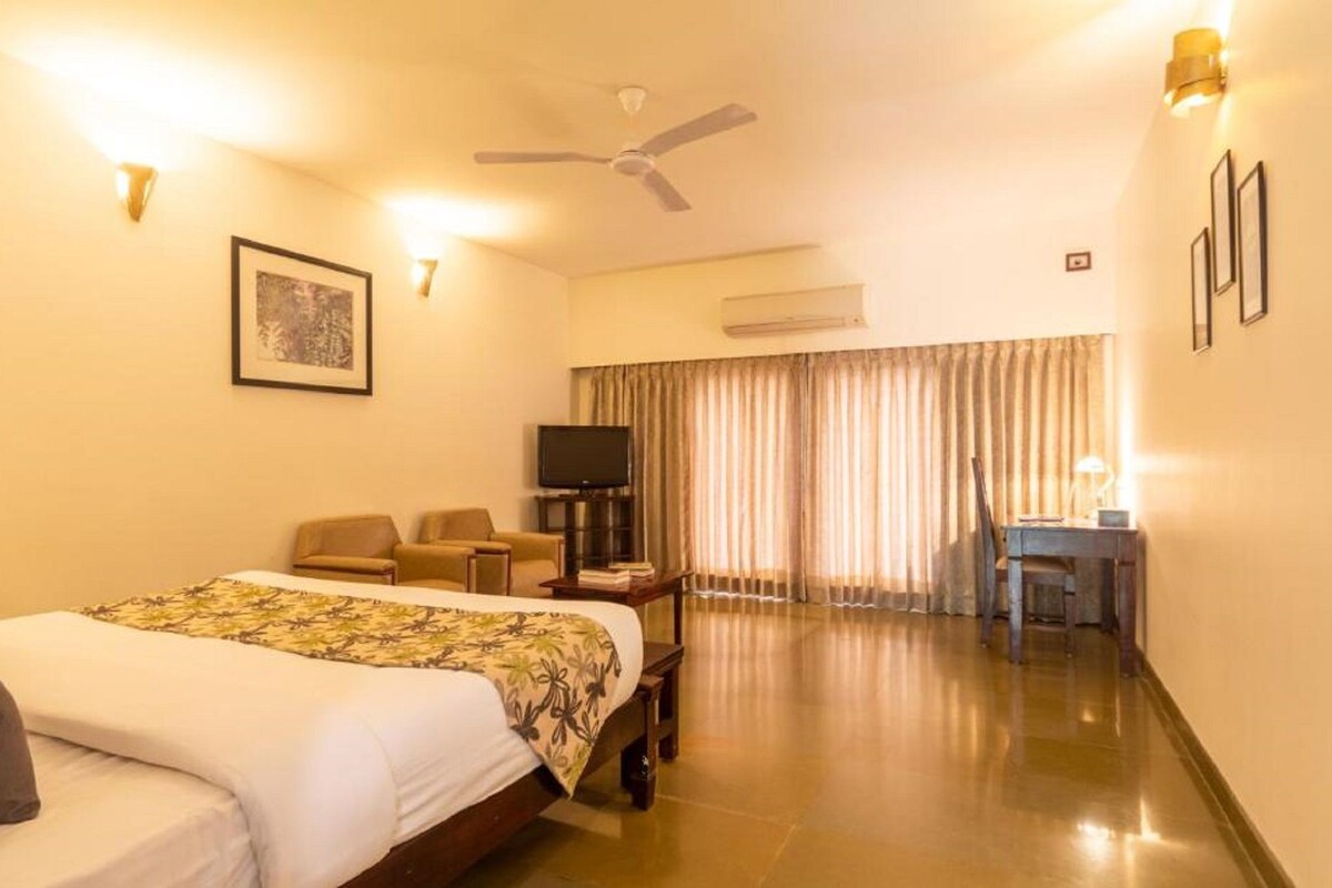 Ein Hotelzimmer mit Bett, Schreibtisch, Stuhl, Fernseher und Deckenventilator.