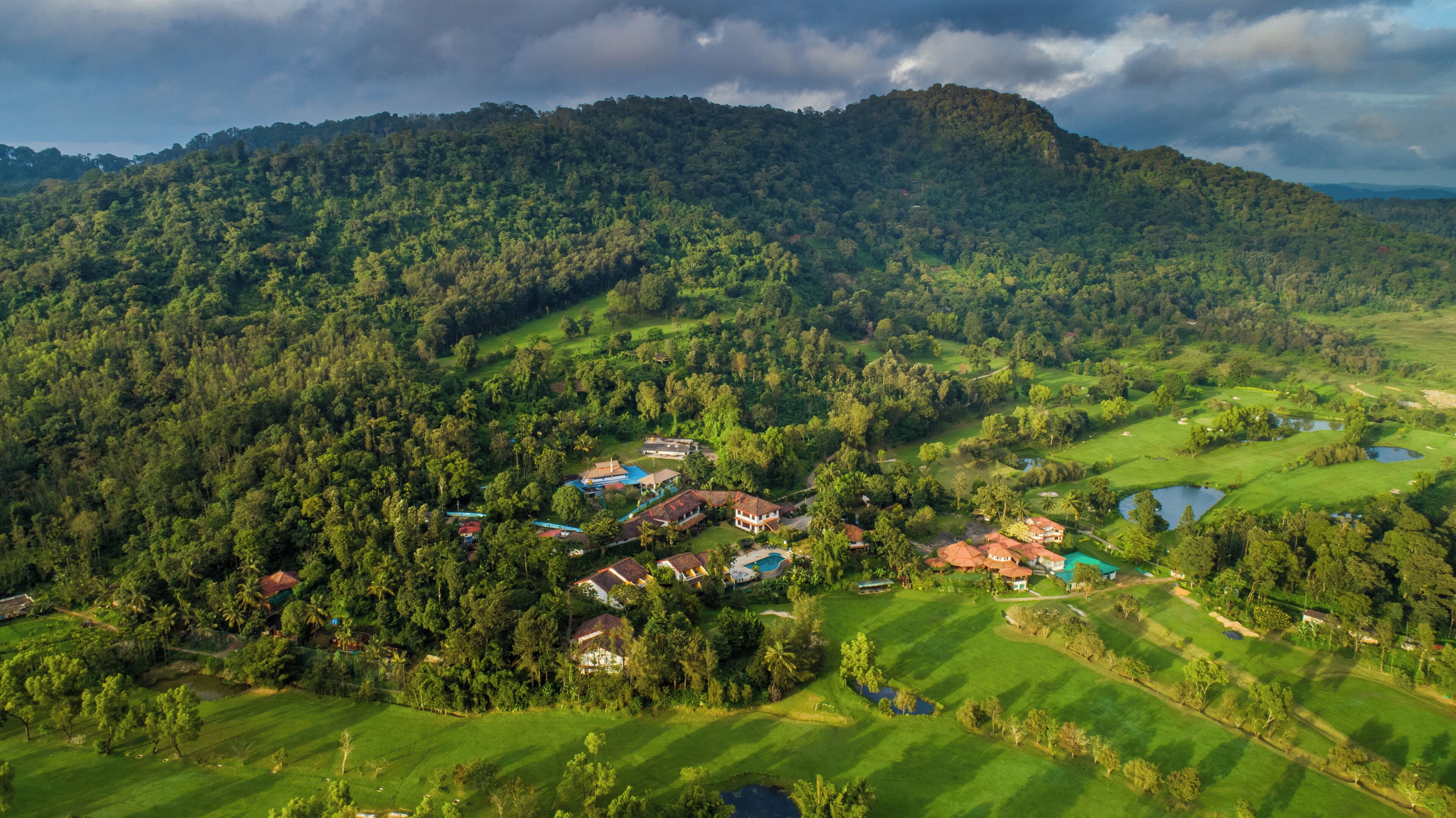 Un paysage verdoyant et luxuriant, avec un terrain de golf, plusieurs maisons et une grande colline en arrière-plan.