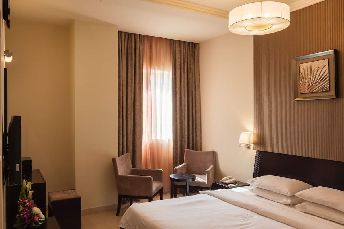 Une chambre d’hôtel avec un grand lit, deux fauteuils, une petite table, un téléviseur et un tableau au mur.