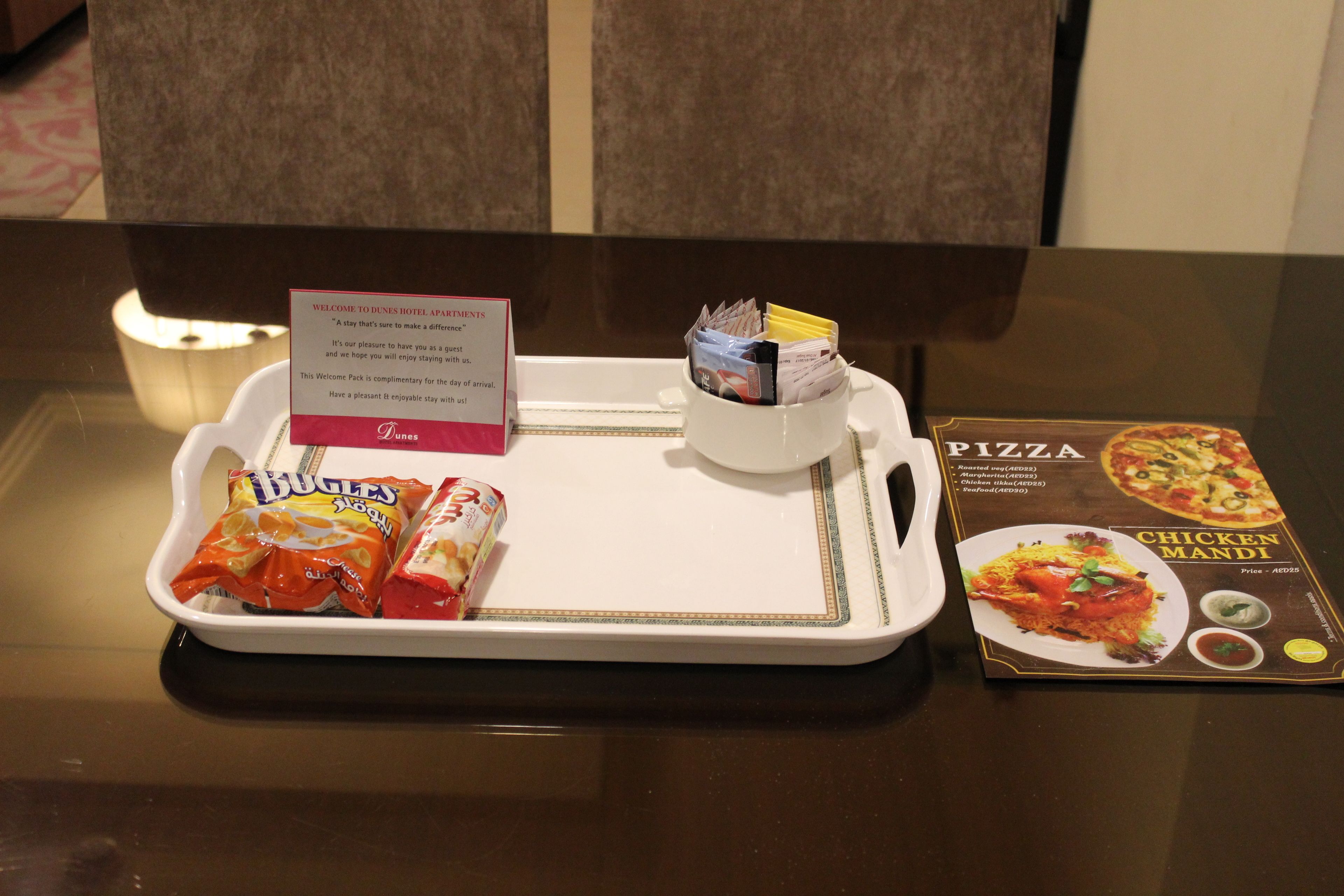 A welcome pack with snacks and a pizza menu on a hotel table.