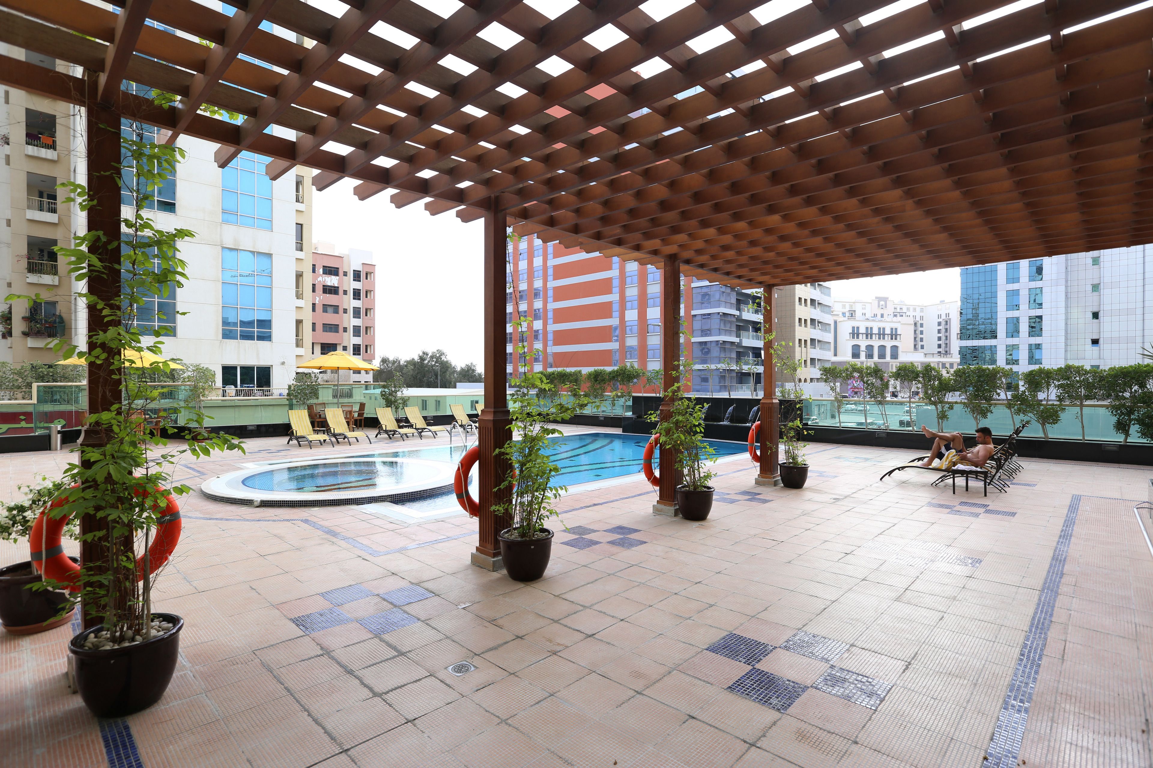 Un área de piscina al aire libre con un pérgola de madera, plantas en macetas y sillas de descanso.