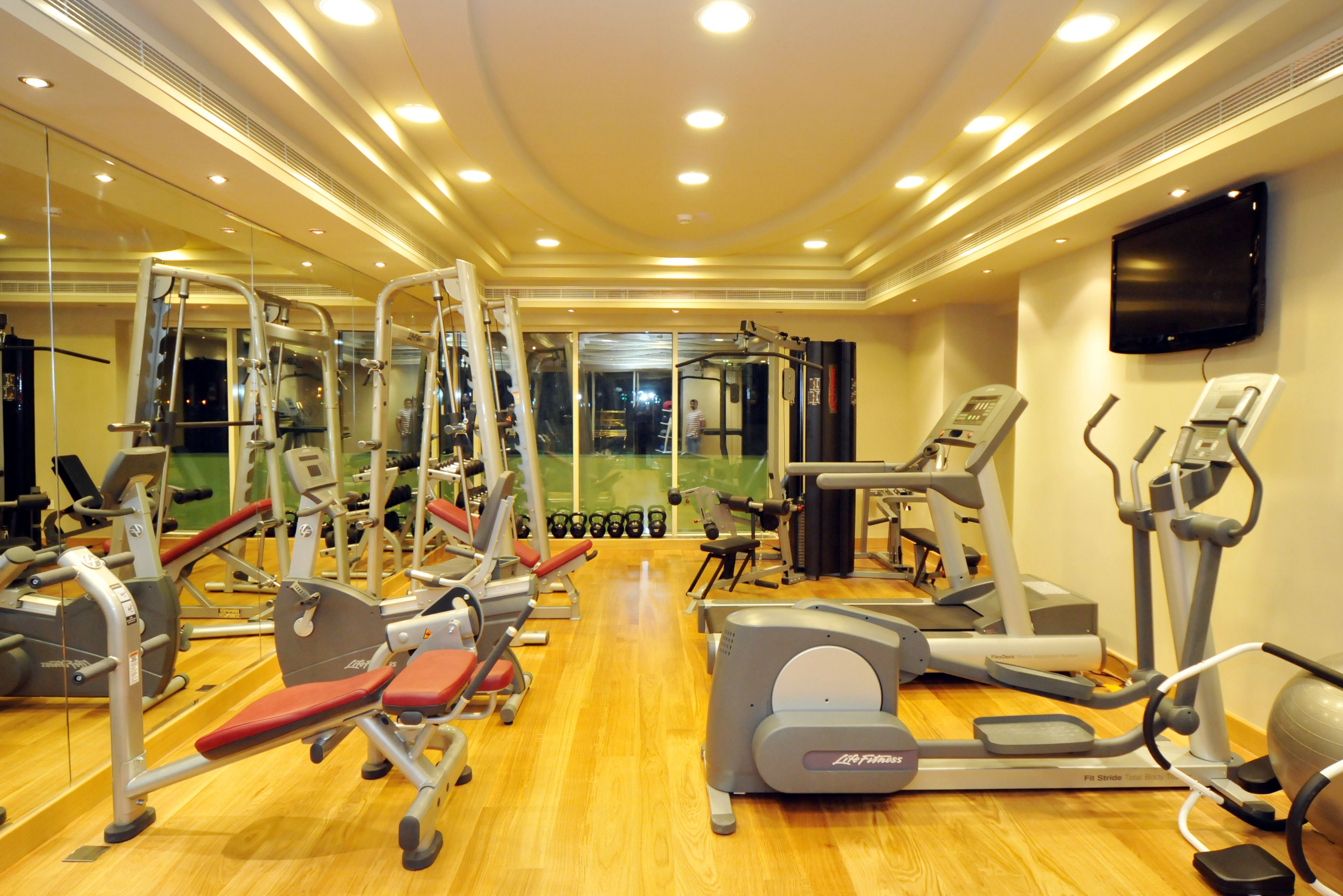 Une salle de sport équipée de divers appareils d’exercice, avec un miroir et un téléviseur accroché au mur.