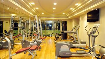 Une salle de sport équipée de divers appareils d’exercice, avec un miroir et un téléviseur accroché au mur.