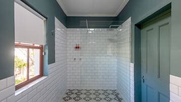 A bathroom with white tiled walls, a shower with a glass door, and a window with a wooden frame.
