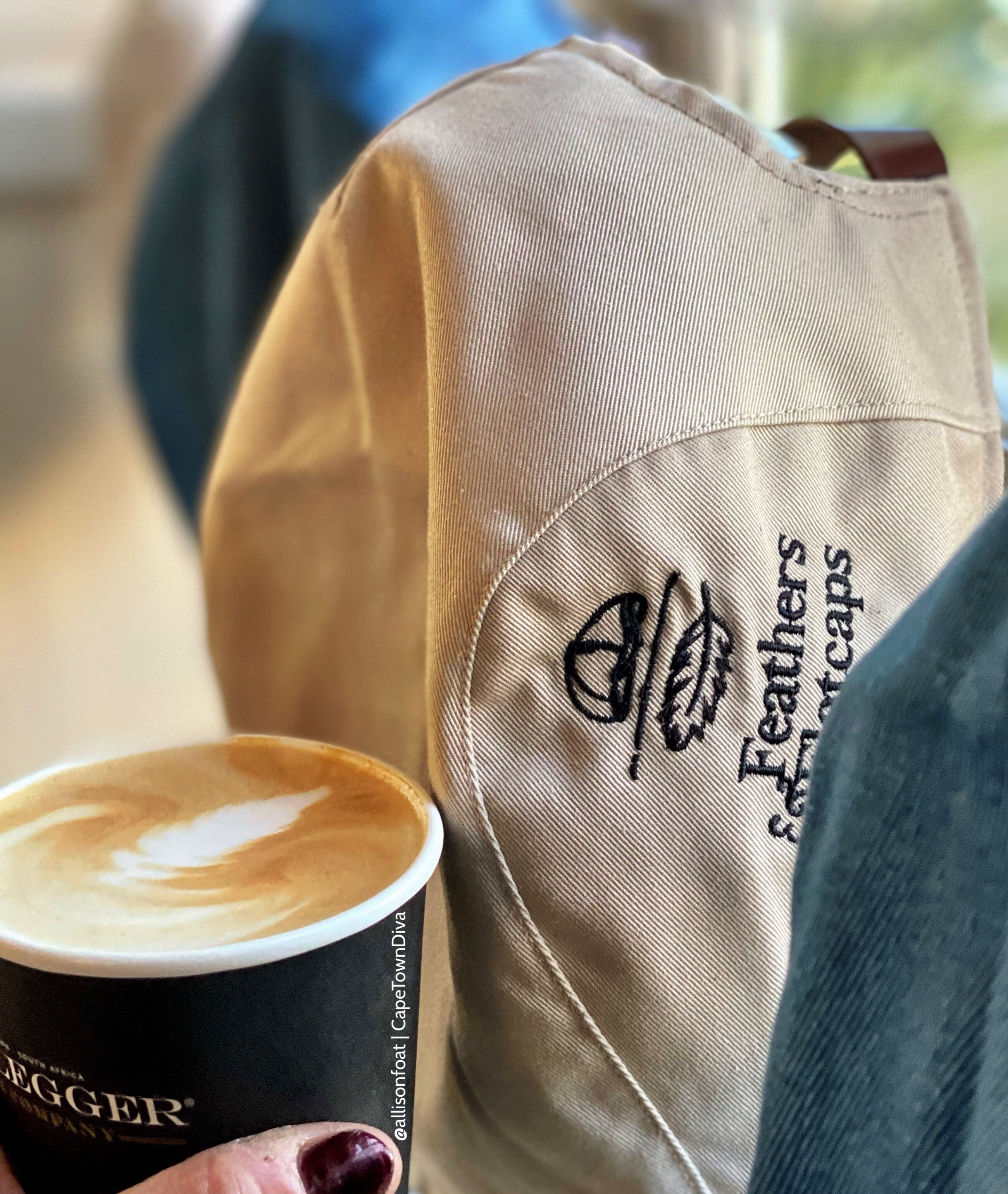 A person holding a cup of coffee with a logo on the cup and a cap with embroidered text.