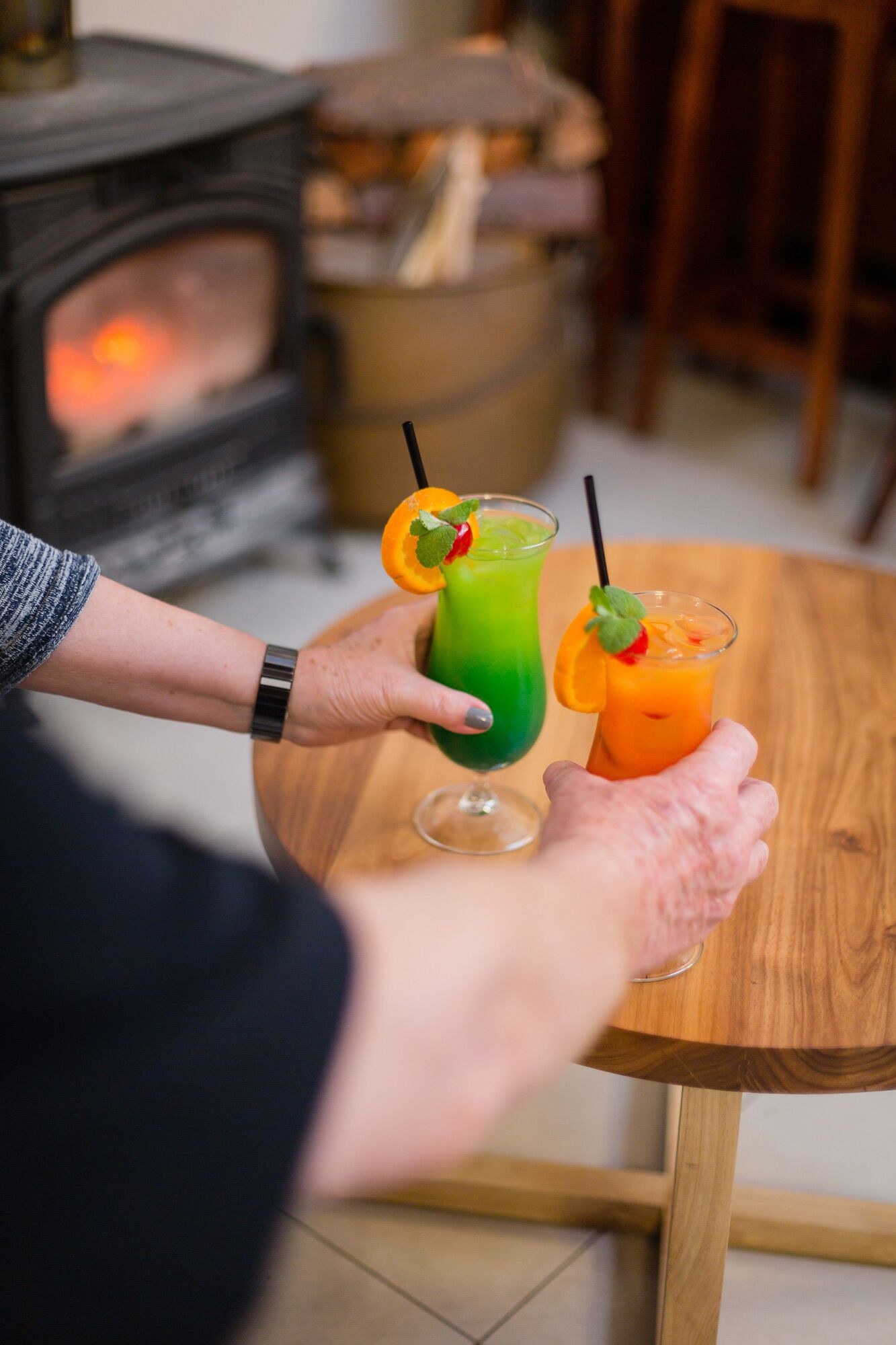 Une personne tenant deux verres de boissons sur une table en bois.