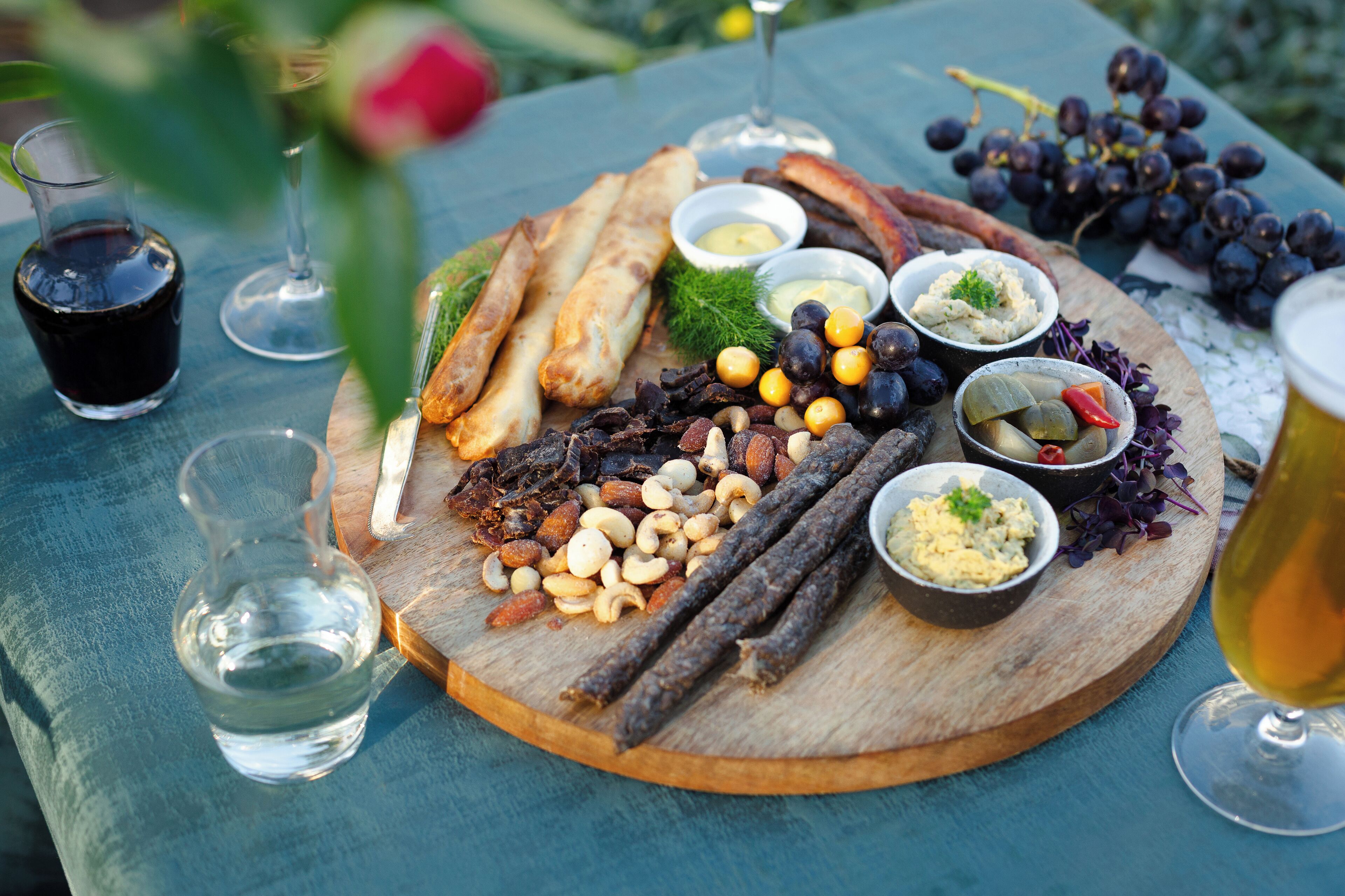 Un tagliere di legno con diversi formaggi, noci e frutta, accompagnato da bicchieri di vino e una bottiglia d'acqua.