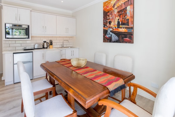 Une cuisine moderne avec des meubles blancs, un four encastré et un coin repas comprenant une table et des chaises en bois.