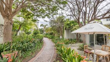 A garden pathway with a brick walkway, surrounded by lush greenery and flowering plants.